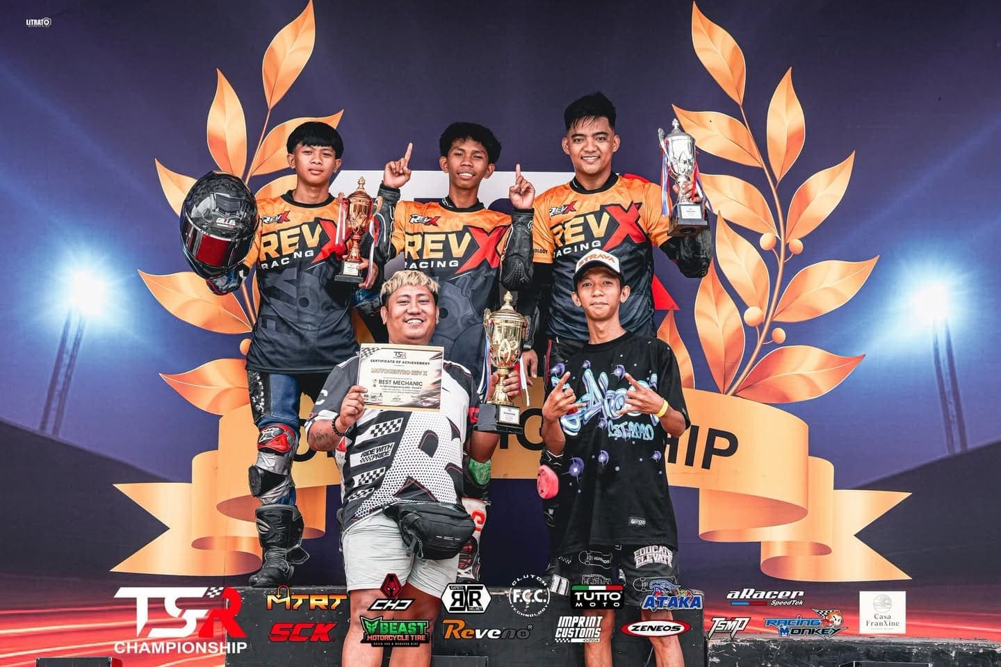 Three RevX Racing riders on a TSR Championship podium holding their trophies, with a Best Mechanic certificate held up in front of them