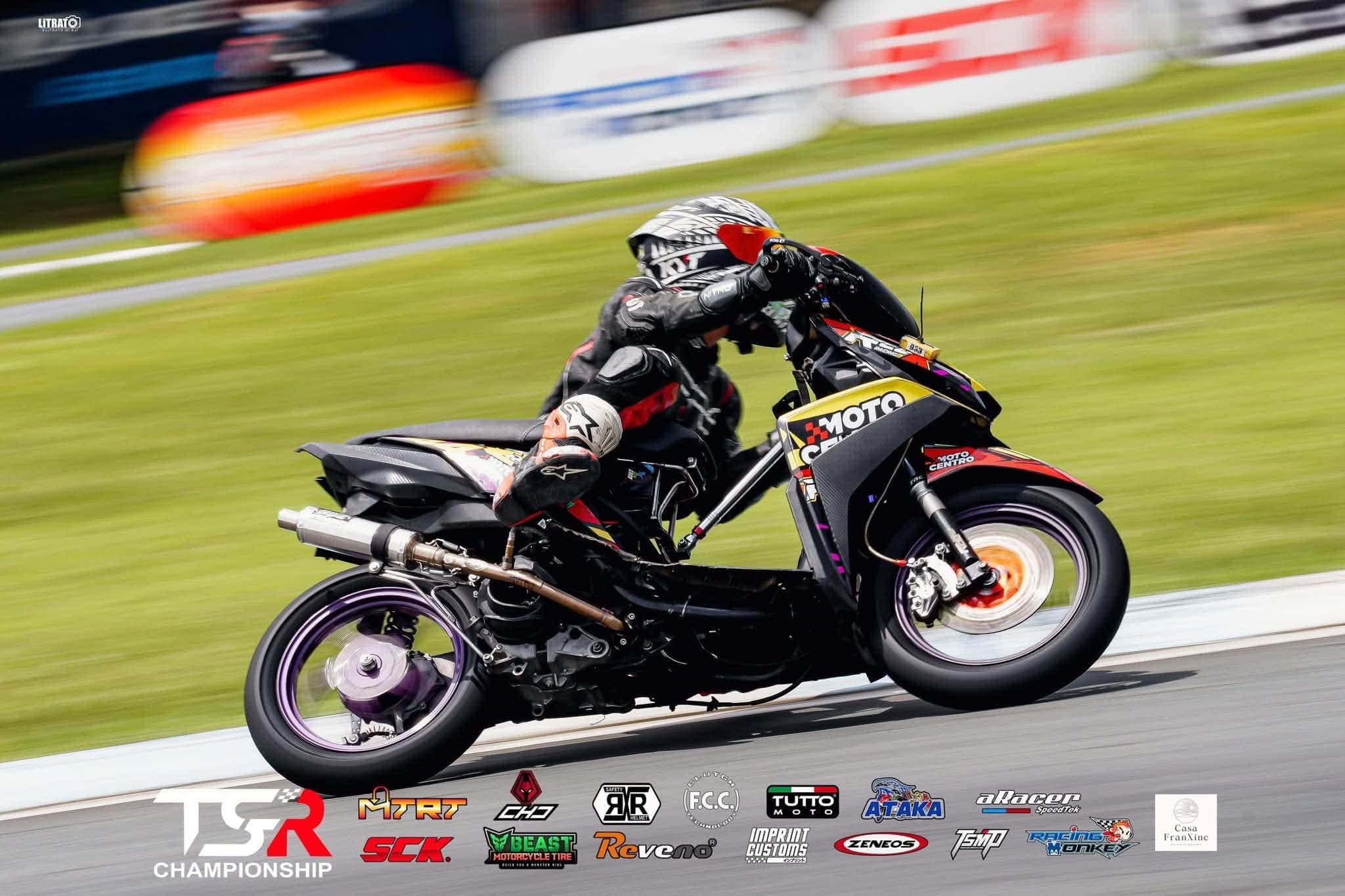 A rider tucked in behind a Motocentro-liveried scooter at speed, panned
